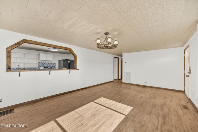 unfurnished living room featuring an inviting chandelier, wood-type flooring, and visible vents