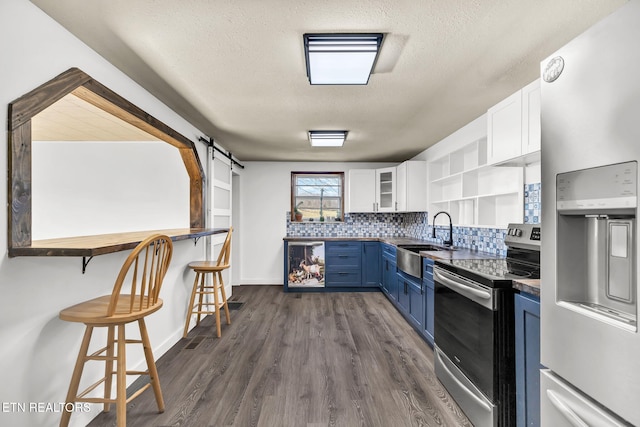 kitchen featuring open shelves, stainless steel appliances, a barn door, a sink, and blue cabinets