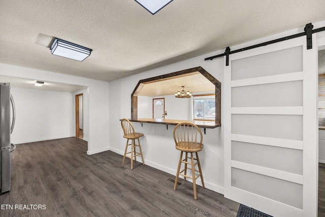 kitchen with dark wood-style floors, a textured ceiling, a breakfast bar area, and a barn door