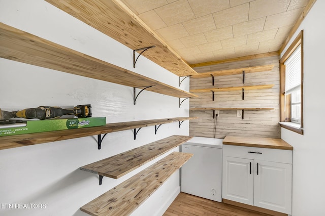 interior space featuring light wood-style floors, wooden walls, and refrigerator