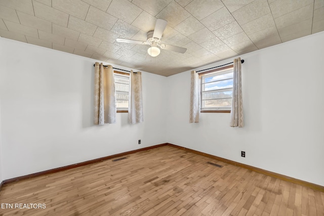 unfurnished room featuring plenty of natural light, wood finished floors, visible vents, and baseboards