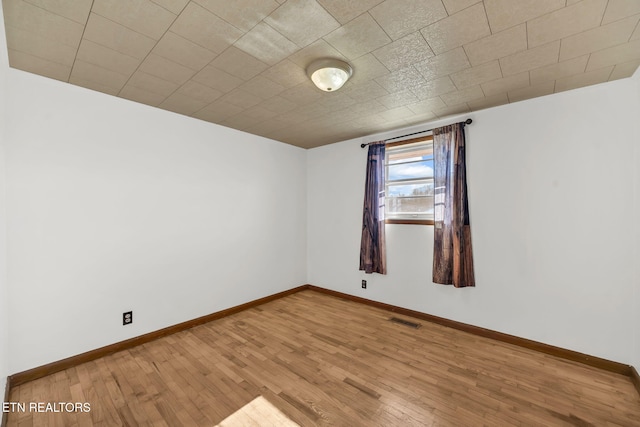 unfurnished room with wood finished floors, visible vents, and baseboards