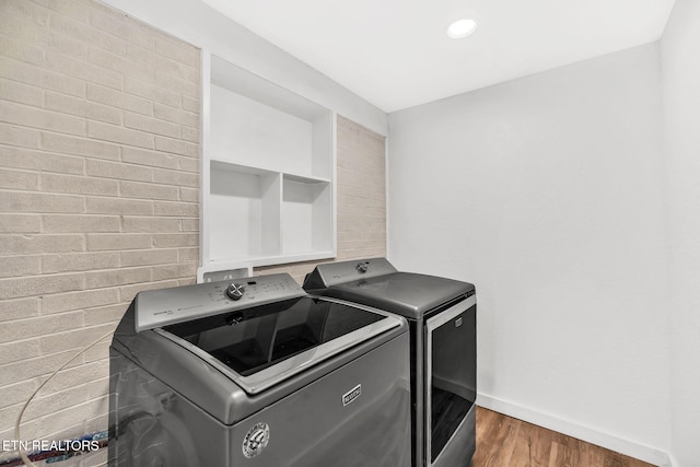 laundry room with washer and clothes dryer, brick wall, wood finished floors, laundry area, and baseboards