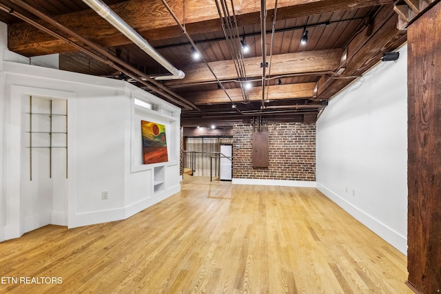 unfurnished living room with wooden ceiling, electric panel, light hardwood / wood-style floors, and brick wall