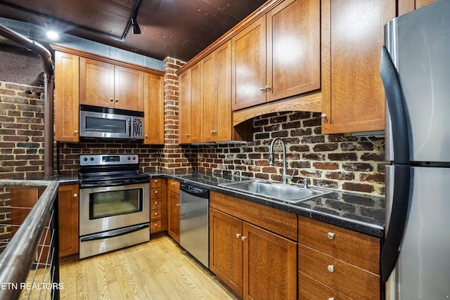 kitchen with dark stone counters, track lighting, sink, light wood-type flooring, and appliances with stainless steel finishes