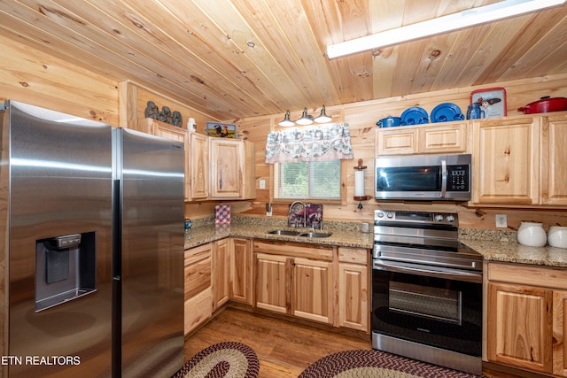 kitchen featuring wood walls, sink, appliances with stainless steel finishes, light hardwood / wood-style floors, and light stone counters