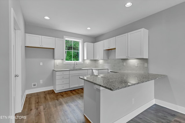 kitchen featuring kitchen peninsula, white cabinetry, sink, and stone countertops