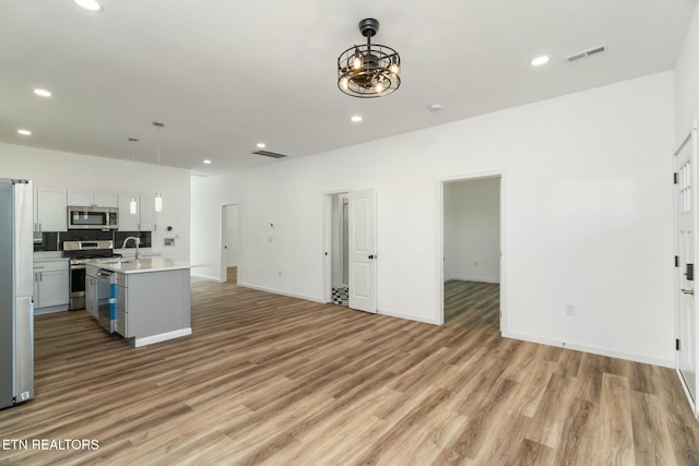 kitchen with hanging light fixtures, stainless steel appliances, a center island with sink, light wood-type flooring, and white cabinets