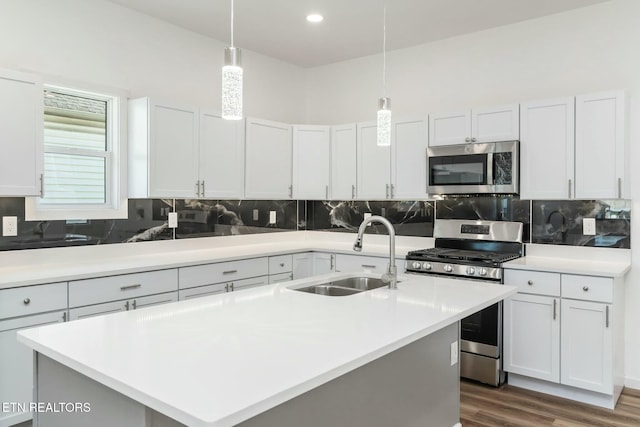 kitchen with stainless steel appliances, sink, white cabinetry, an island with sink, and hanging light fixtures