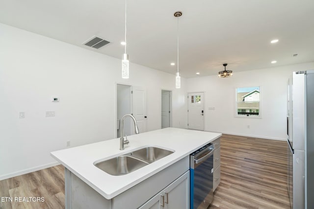 kitchen featuring stainless steel dishwasher, hanging light fixtures, a center island with sink, light wood-type flooring, and sink