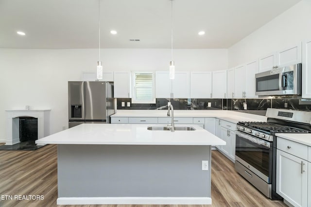 kitchen featuring decorative light fixtures, stainless steel appliances, an island with sink, white cabinets, and sink