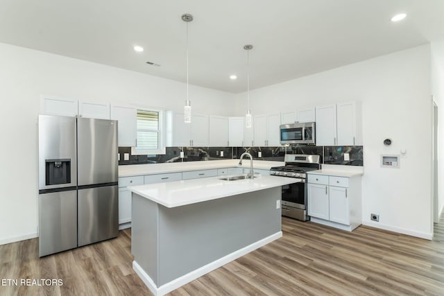 kitchen with a kitchen island with sink, appliances with stainless steel finishes, pendant lighting, white cabinets, and sink