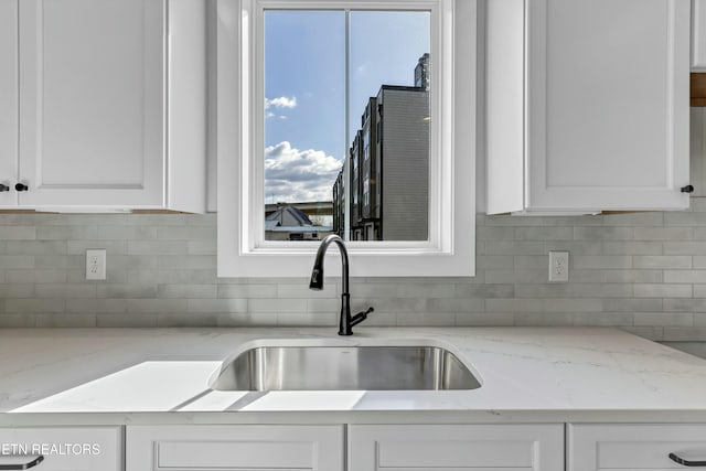 kitchen featuring light stone counters, white cabinetry, sink, and tasteful backsplash