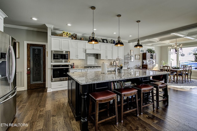 kitchen with a large island with sink, crown molding, decorative light fixtures, white cabinets, and appliances with stainless steel finishes