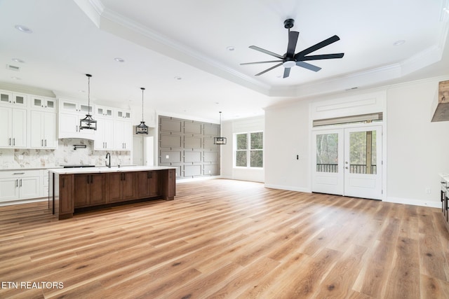 kitchen with a tray ceiling, a center island with sink, white cabinets, and light wood-type flooring