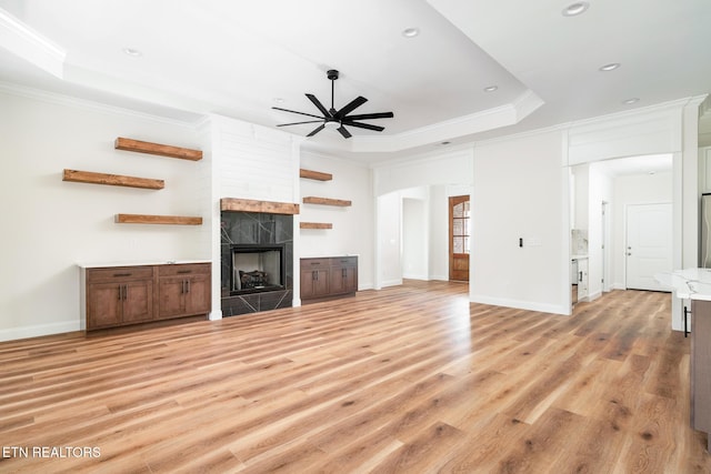 unfurnished living room featuring a raised ceiling, crown molding, light hardwood / wood-style flooring, ceiling fan, and a tiled fireplace