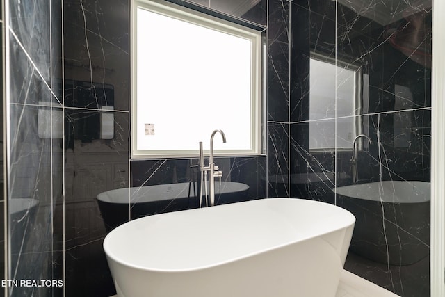 bathroom with a bathtub, a healthy amount of sunlight, and tile walls