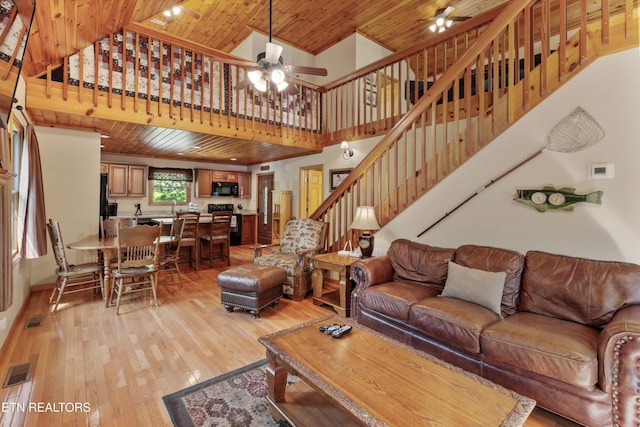 living room with ceiling fan, light wood-type flooring, wooden ceiling, and a towering ceiling