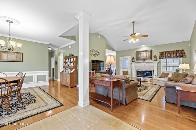 living room with a tiled fireplace, ceiling fan with notable chandelier, ornate columns, and light hardwood / wood-style floors