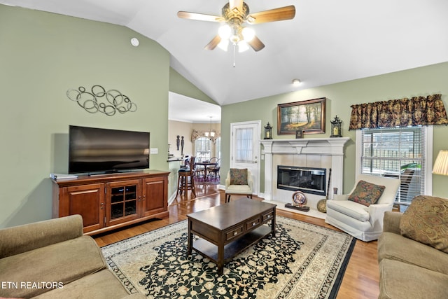 living room featuring ceiling fan with notable chandelier, a tile fireplace, lofted ceiling, and light hardwood / wood-style flooring