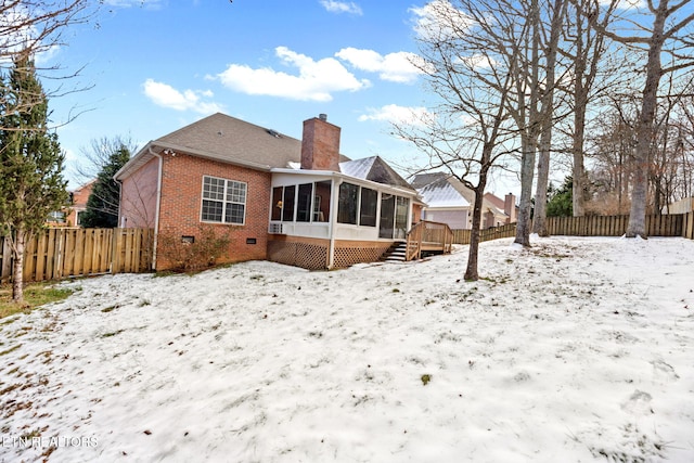 snow covered rear of property with a sunroom