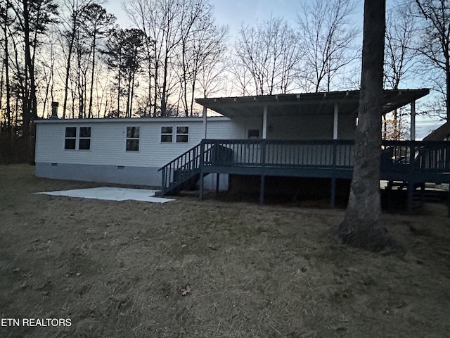 back house at dusk with a lawn and a deck