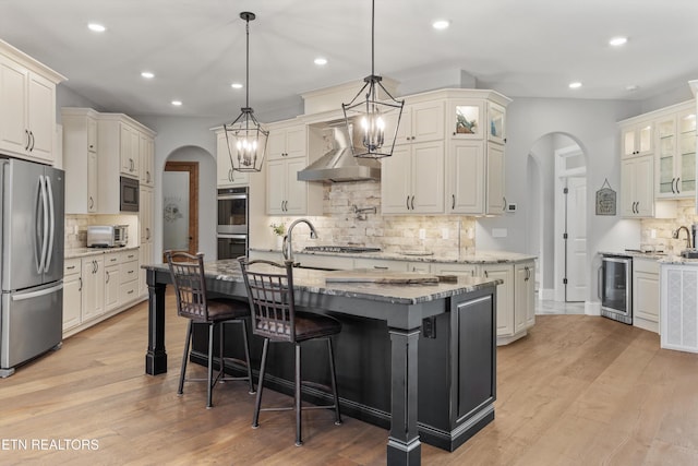 kitchen with a center island with sink, stainless steel appliances, tasteful backsplash, beverage cooler, and wall chimney exhaust hood