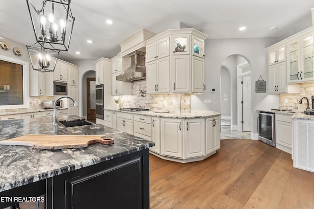 kitchen featuring appliances with stainless steel finishes, decorative light fixtures, wine cooler, wall chimney exhaust hood, and sink