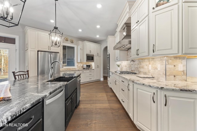 kitchen with white cabinetry, stainless steel appliances, dark hardwood / wood-style floors, decorative light fixtures, and wall chimney exhaust hood