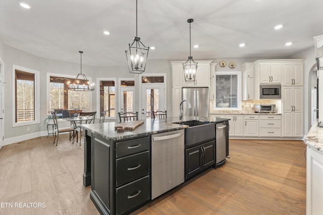 kitchen featuring white cabinetry, stainless steel appliances, decorative backsplash, a kitchen island with sink, and decorative light fixtures