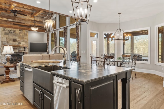 kitchen featuring ceiling fan, pendant lighting, light hardwood / wood-style flooring, an island with sink, and a stone fireplace