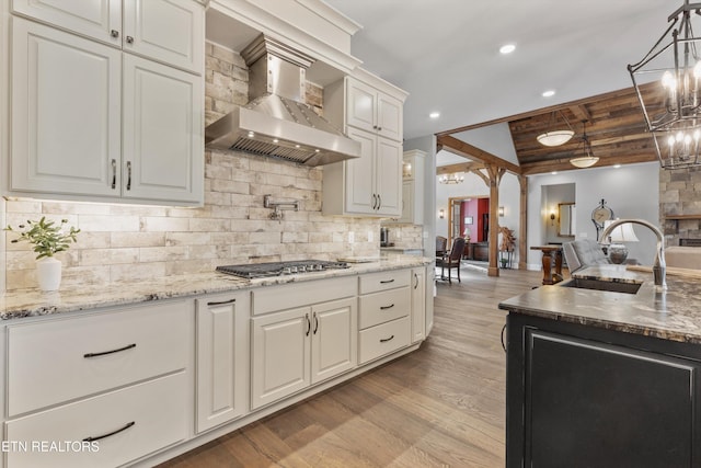 kitchen featuring wall chimney range hood, vaulted ceiling with beams, sink, stainless steel gas cooktop, and wooden ceiling