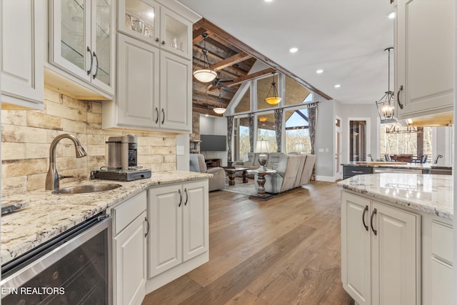 kitchen with tasteful backsplash, wine cooler, hanging light fixtures, white cabinets, and sink