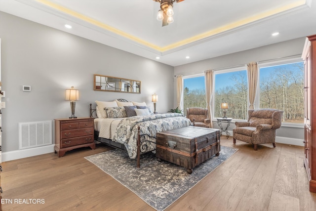 bedroom featuring ceiling fan, multiple windows, a tray ceiling, and light wood-type flooring