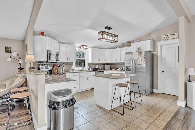 kitchen featuring a kitchen bar, sink, a center island, stainless steel appliances, and white cabinets