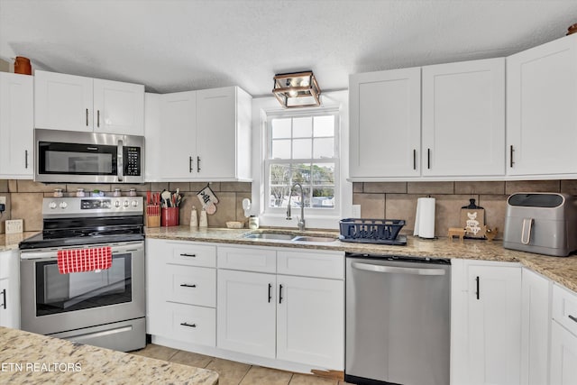 kitchen featuring appliances with stainless steel finishes, white cabinetry, sink, decorative backsplash, and light tile patterned floors