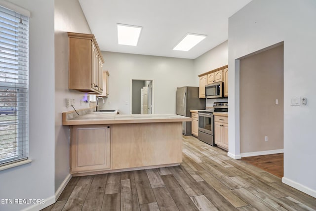 kitchen featuring light brown cabinets, sink, stainless steel appliances, kitchen peninsula, and light wood-type flooring