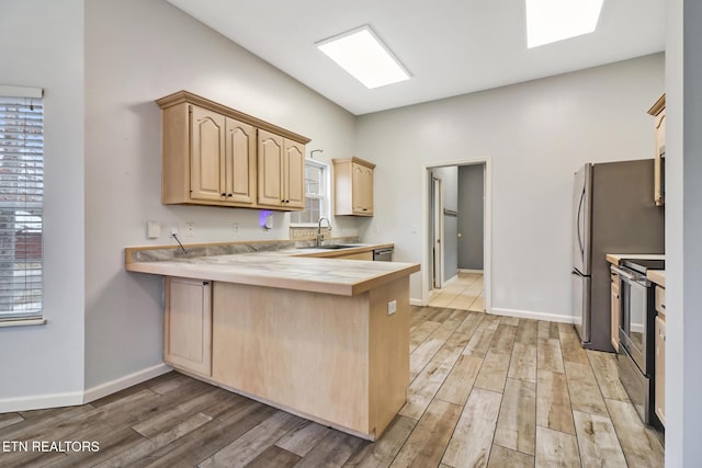 kitchen with kitchen peninsula, light brown cabinetry, stainless steel appliances, and light wood-type flooring