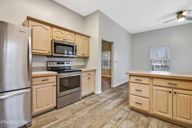 kitchen with stainless steel appliances, ceiling fan, light brown cabinets, tile countertops, and light hardwood / wood-style flooring