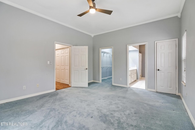 unfurnished bedroom featuring light carpet, ensuite bathroom, ceiling fan, crown molding, and a spacious closet