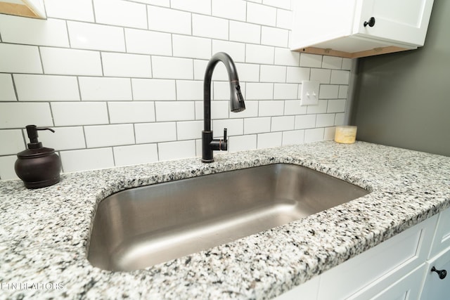 details featuring decorative backsplash, light stone countertops, sink, and white cabinetry