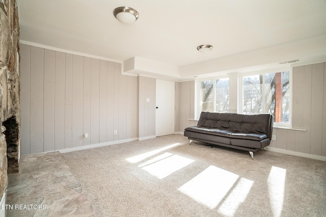 living area featuring light carpet, wood walls, and a stone fireplace