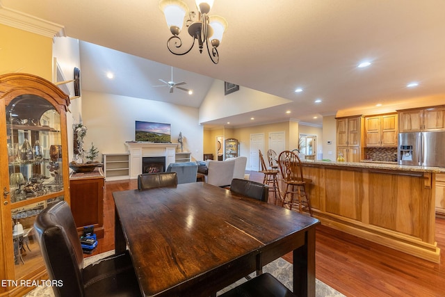 dining space featuring vaulted ceiling, ornamental molding, a fireplace, and wood finished floors