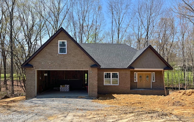 view of front of house with gravel driveway, roof with shingles, covered porch, brick siding, and a garage