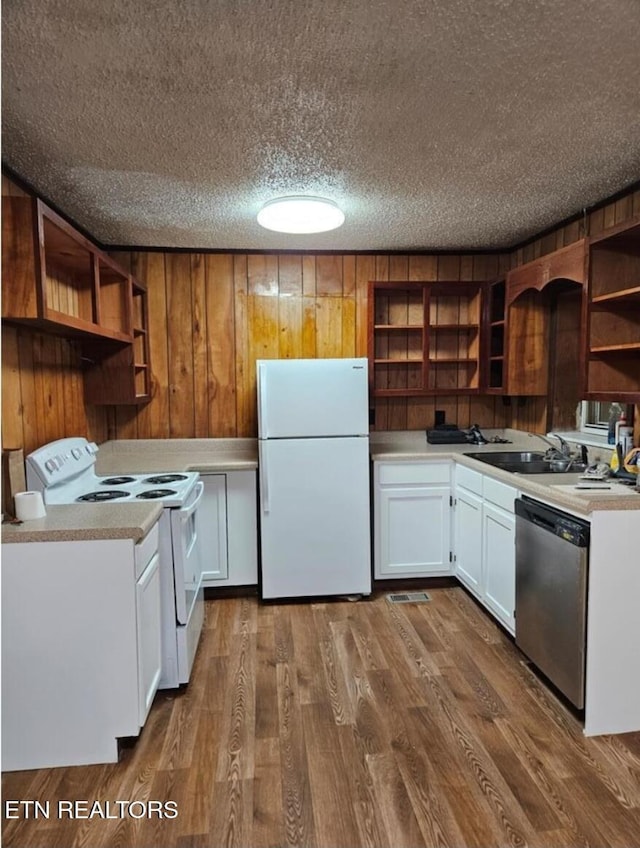 kitchen with hardwood / wood-style floors, wood walls, white appliances, sink, and white cabinetry