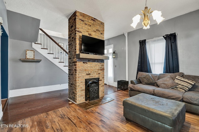 living room featuring a textured ceiling, an inviting chandelier, wood-type flooring, and a brick fireplace