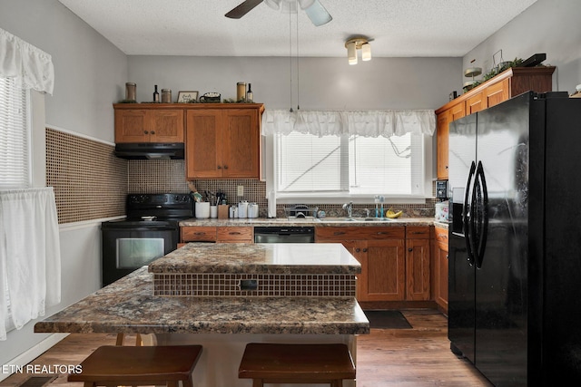 kitchen featuring a textured ceiling, black appliances, a kitchen island, sink, and a breakfast bar area