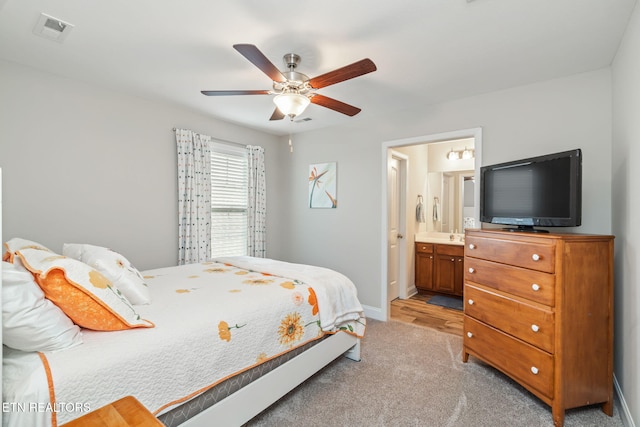 bedroom featuring ceiling fan, light colored carpet, and ensuite bath