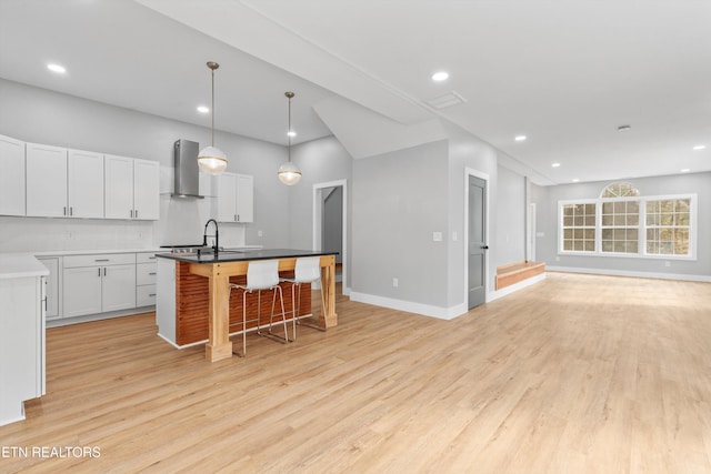 kitchen featuring white cabinetry, a breakfast bar area, a center island with sink, and wall chimney exhaust hood