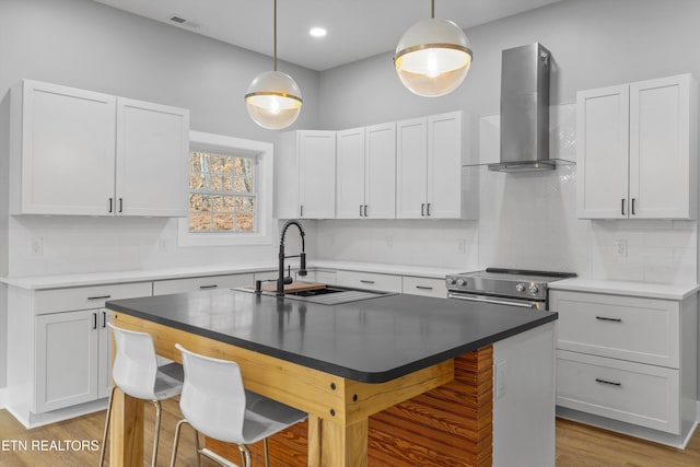 kitchen featuring white cabinetry, sink, stainless steel range with electric cooktop, a kitchen breakfast bar, and wall chimney exhaust hood